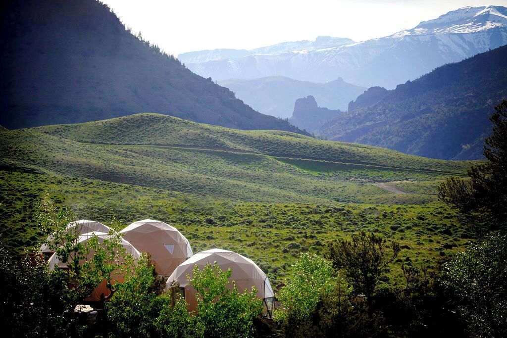 A mountainous landscape with tents in the foreground, suggesting a camping or outdoor accommodation setting.