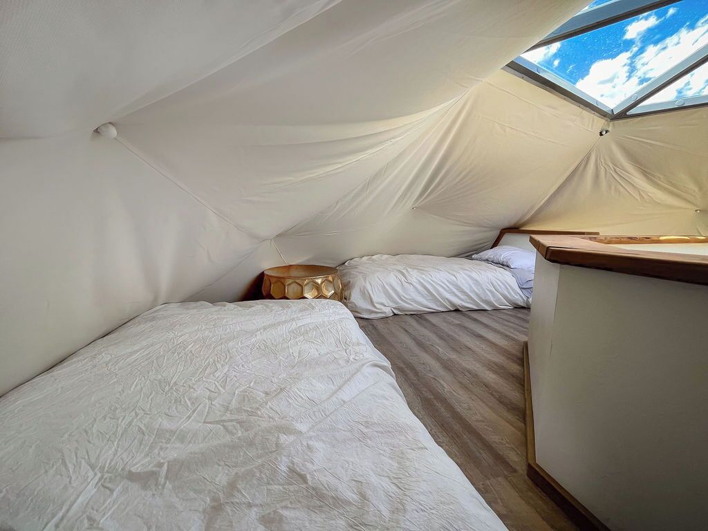 A tented room with two beds, a wooden bench, and a skylight.