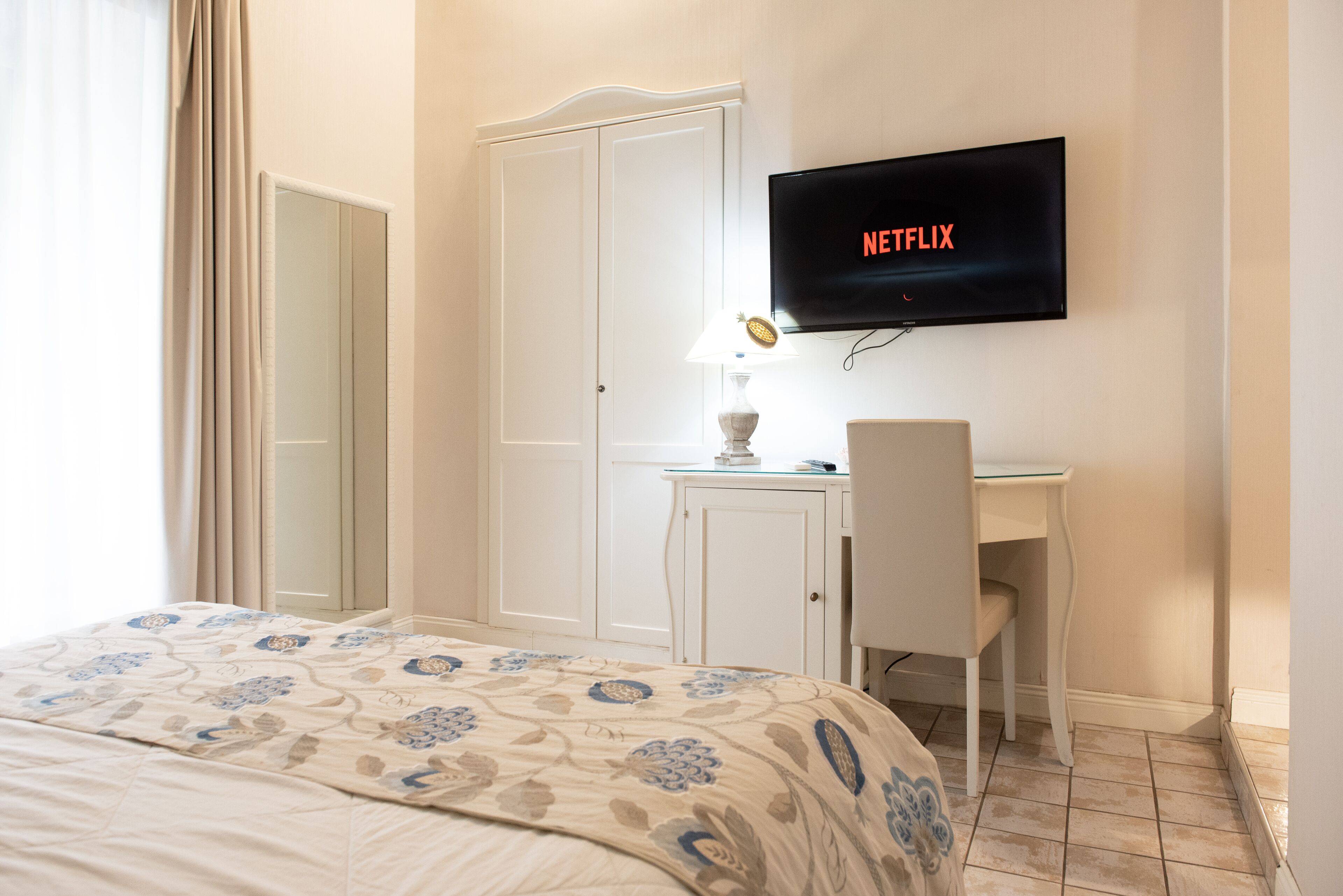 Une chambre d’hôtel avec un lit, un bureau, une chaise, un téléviseur affichant le logo « NETFLIX » et une lampe.