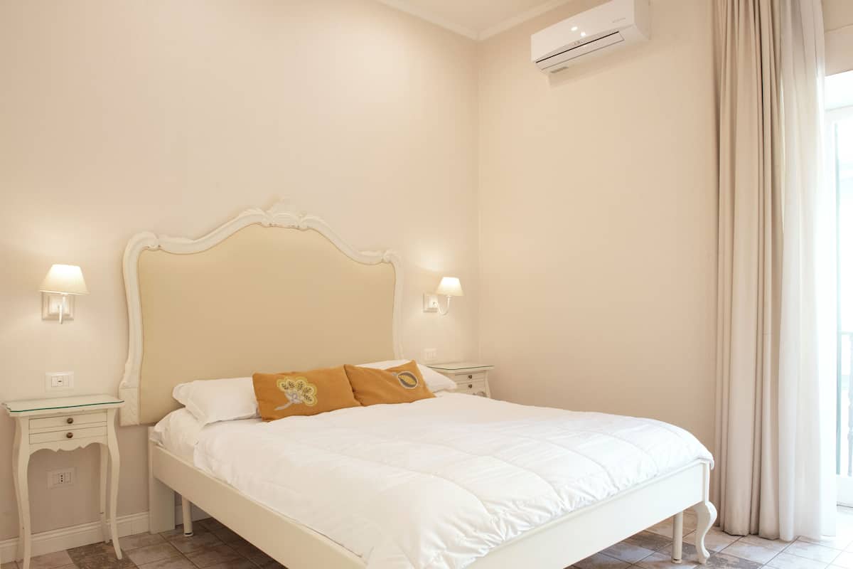 Un dormitorio con una cama blanca, dos mesitas de noche y un aire acondicionado instalado en la pared.