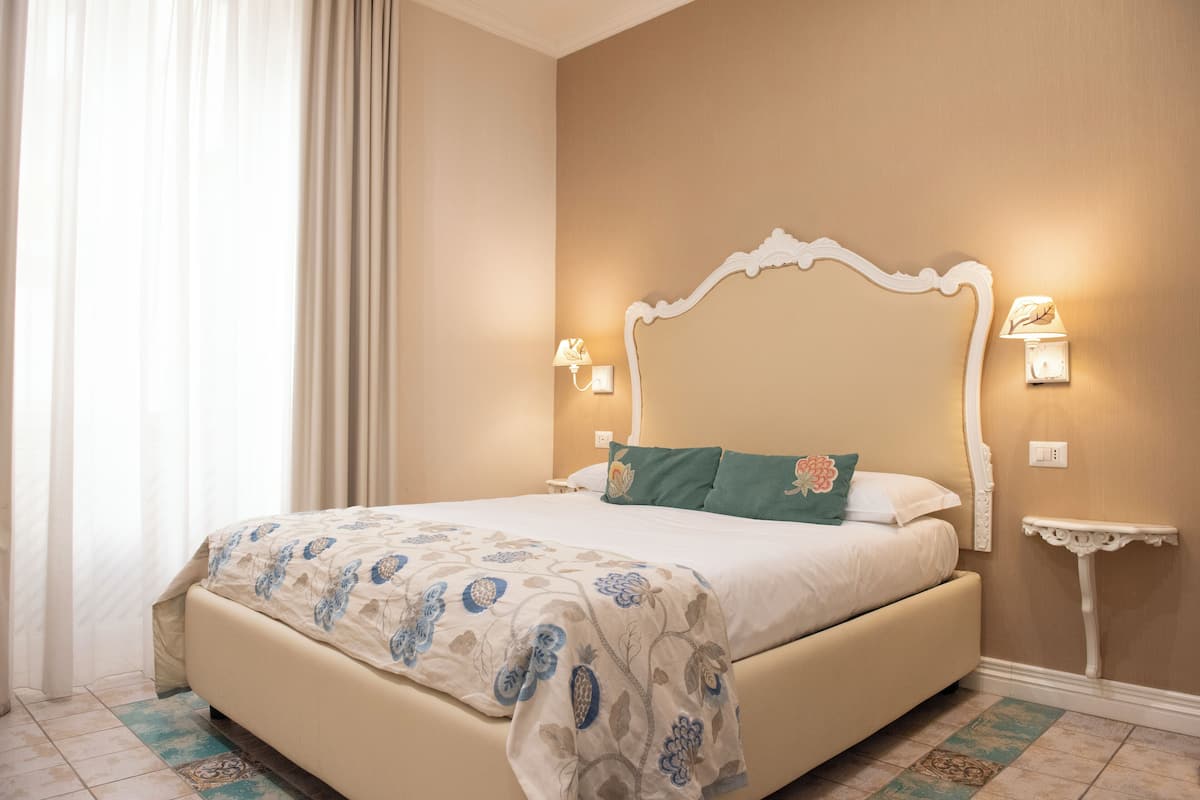 Una cama bien hecha con una colcha de estampado floral, un cabecero blanco y dos lámparas de noche.