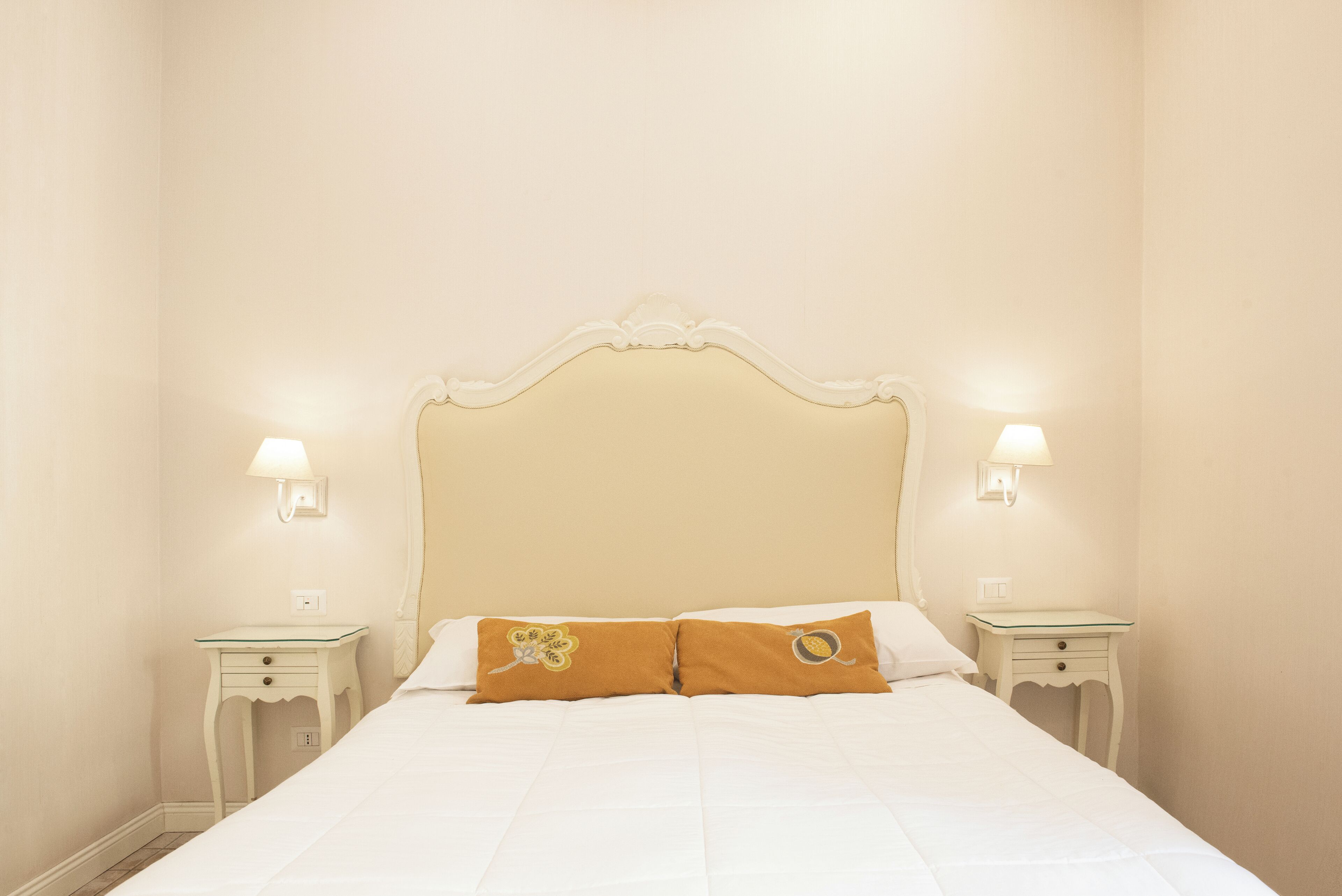 Una cama bien hecha con dos almohadas, dos mesitas de noche y lámparas fijadas a la pared.