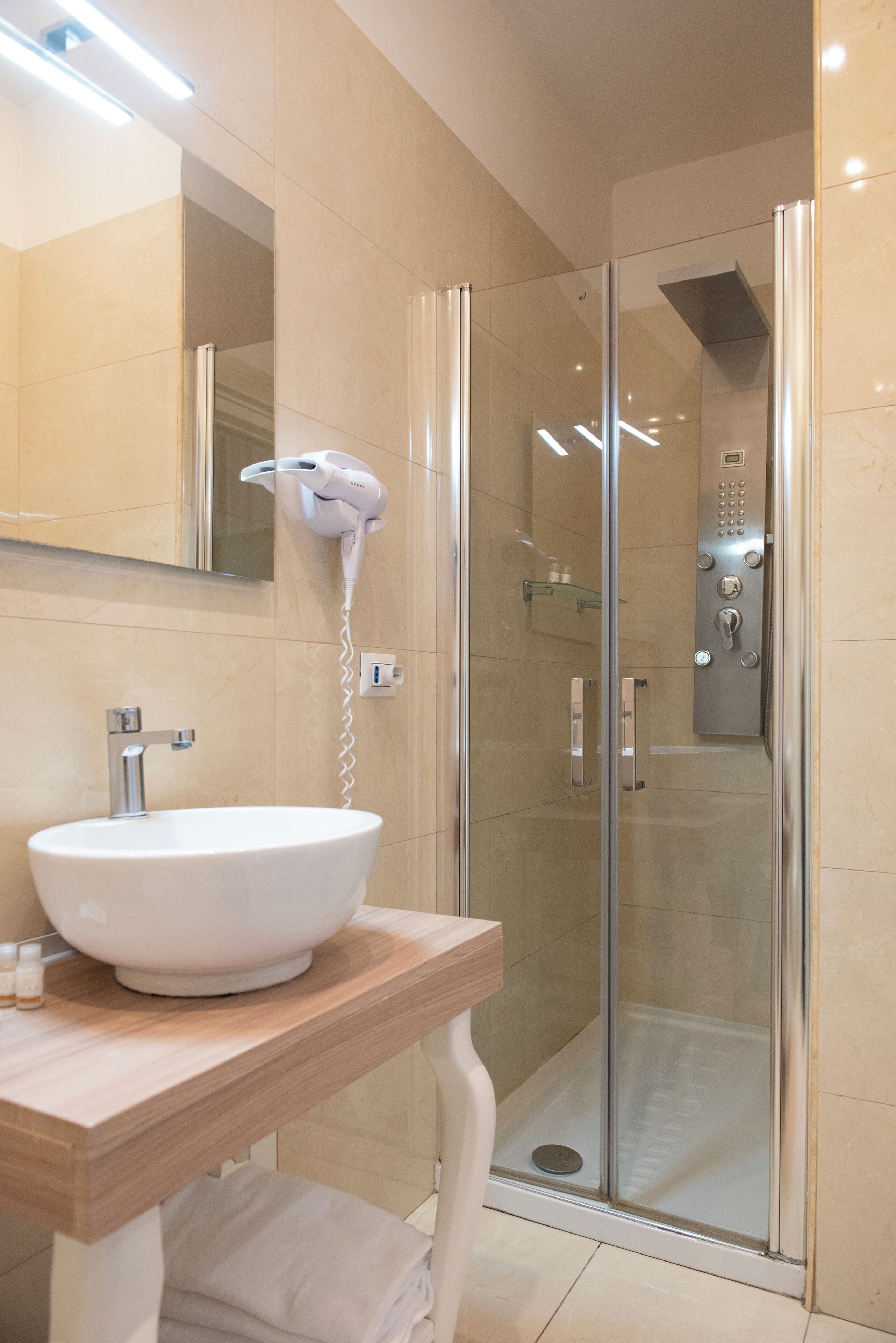 Ein modernes Badezimmer mit einer Duschkabine, einem weißen Waschbecken und einem an der Wand befestigten Föhn.