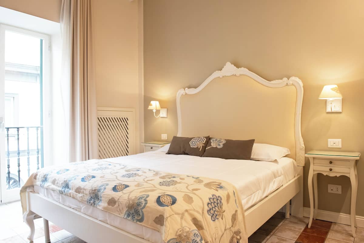 Una cama bien hecha con una colcha estampada con motivos florales, dos lámparas de noche y una mesita de noche con superficie de vidrio.