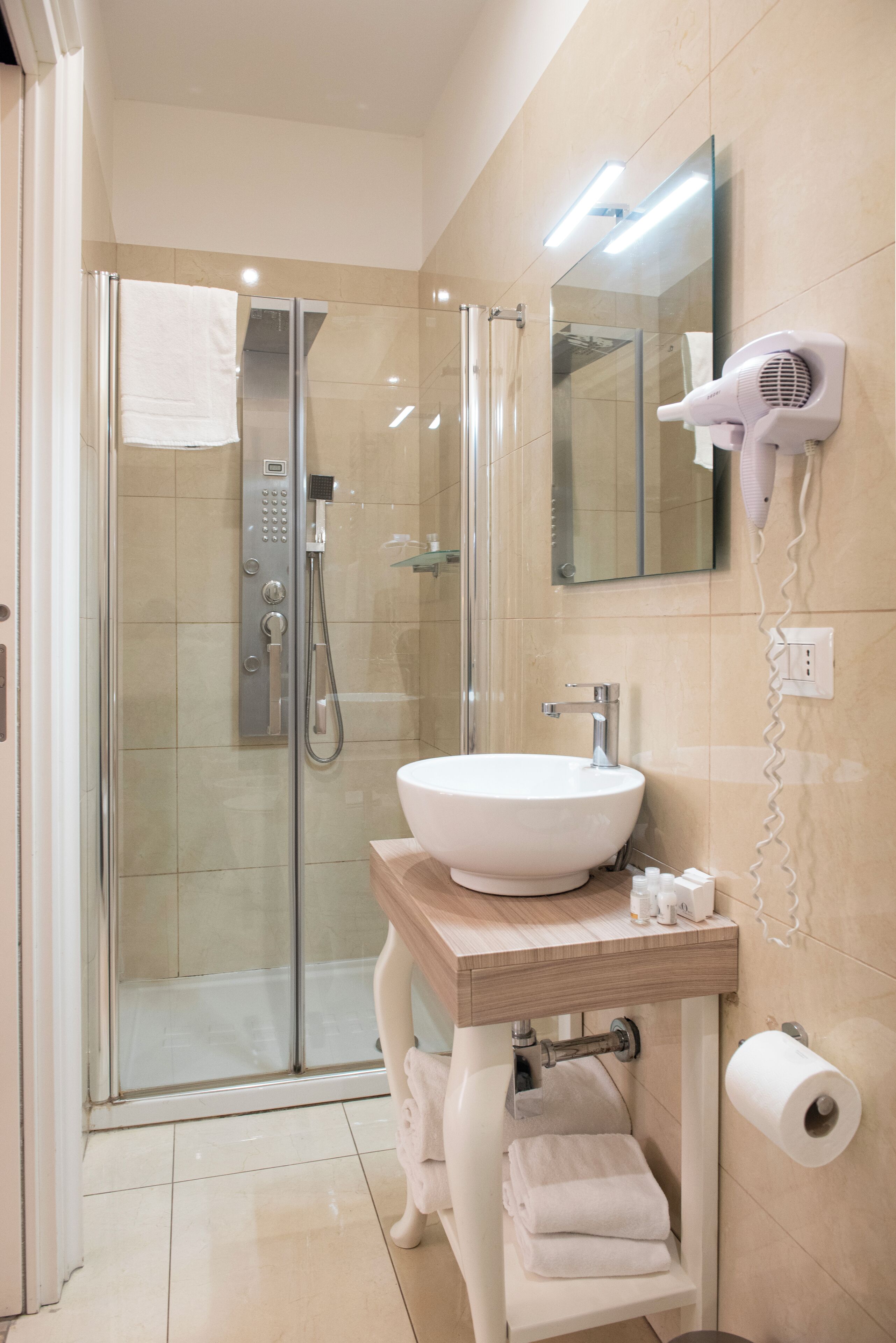 Une salle de bain moderne avec une douche en verre, un lavabo blanc, un sèche-cheveux et un rouleau de papier toilette.