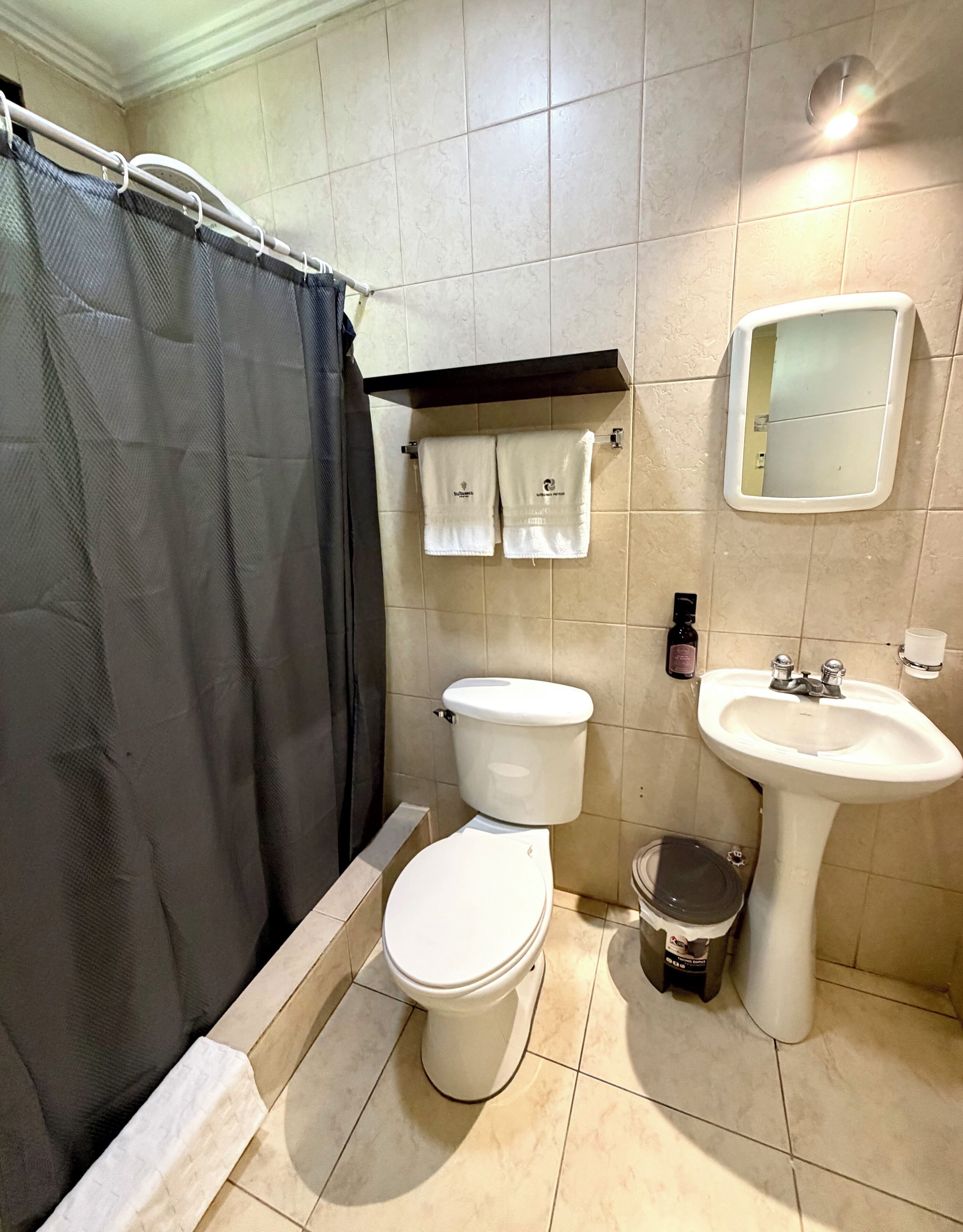 Een badkamer met toilet, wastafel, douchegordijn en handdoeken op een rek.