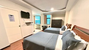 Quarto de hotel com duas camas, televisão, guarda-roupa e vista exterior.