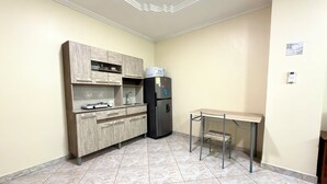 Uma cozinha compacta com fogão embutido, geladeira e uma mesa pequena com uma cadeira.