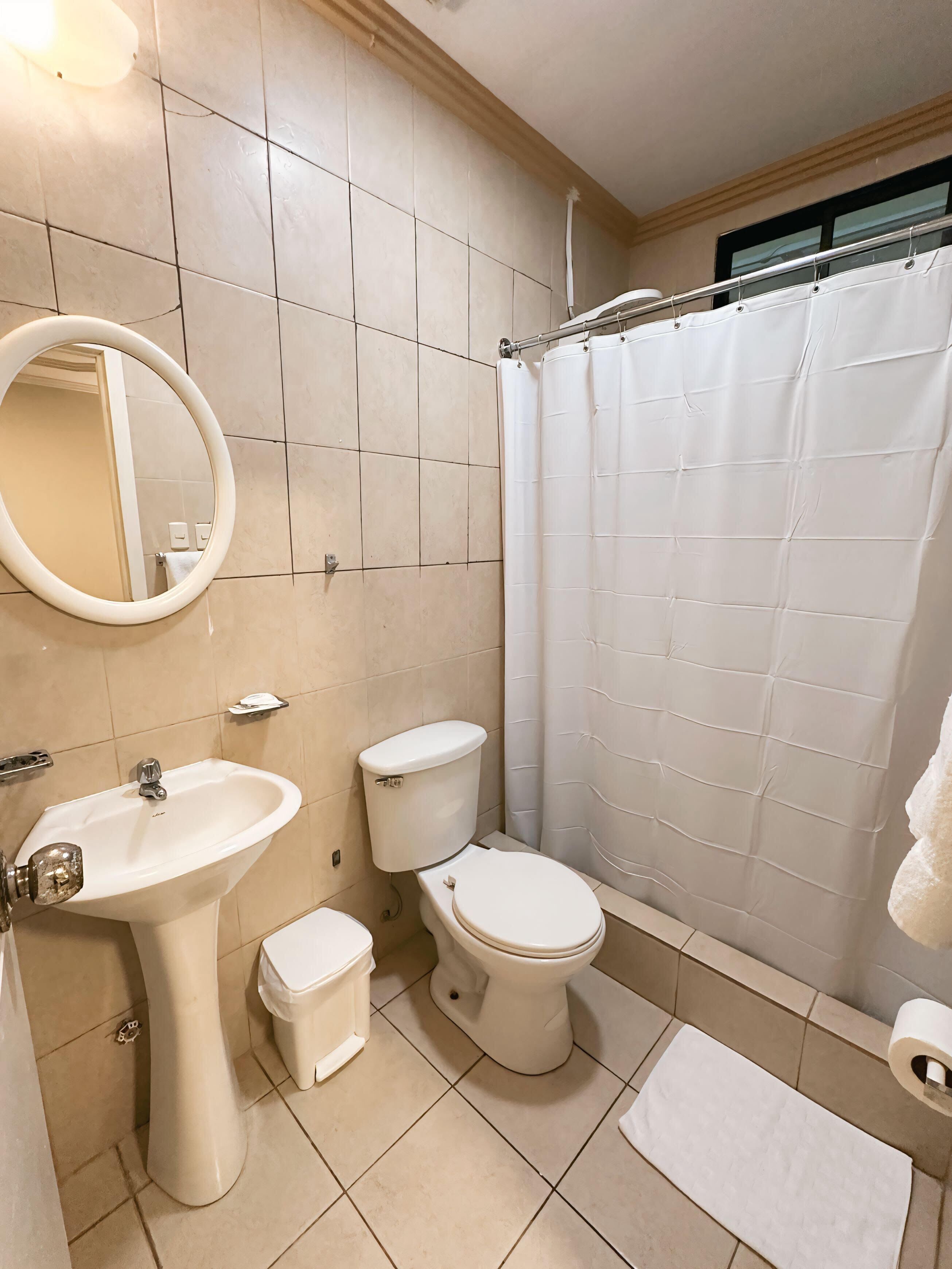 Ein Badezimmer mit Waschbecken, zwei Toiletten, einer Duschvorhang und einem Spiegel.