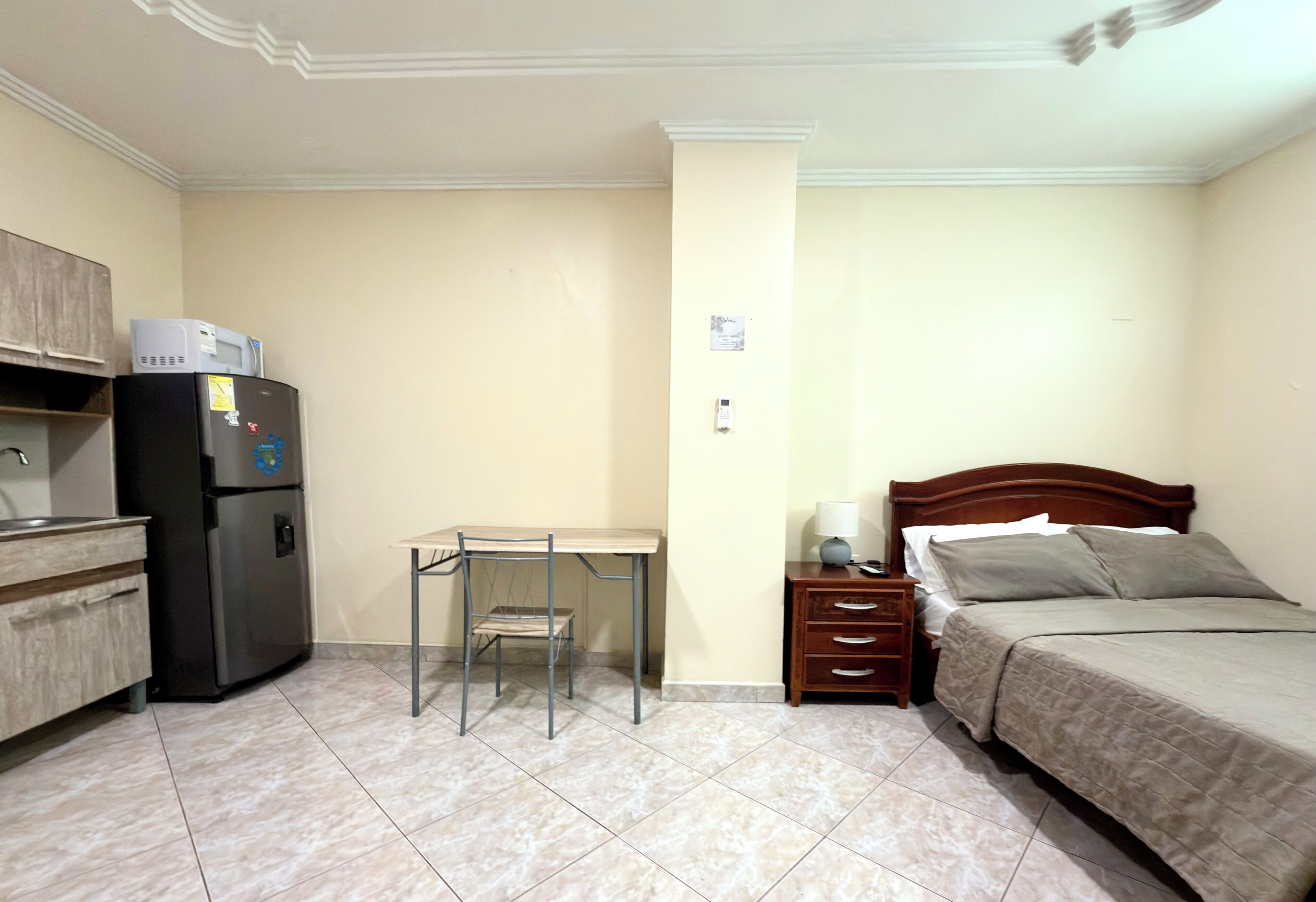 A compact room with a bed, a desk, a refrigerator, and a small cabinet.