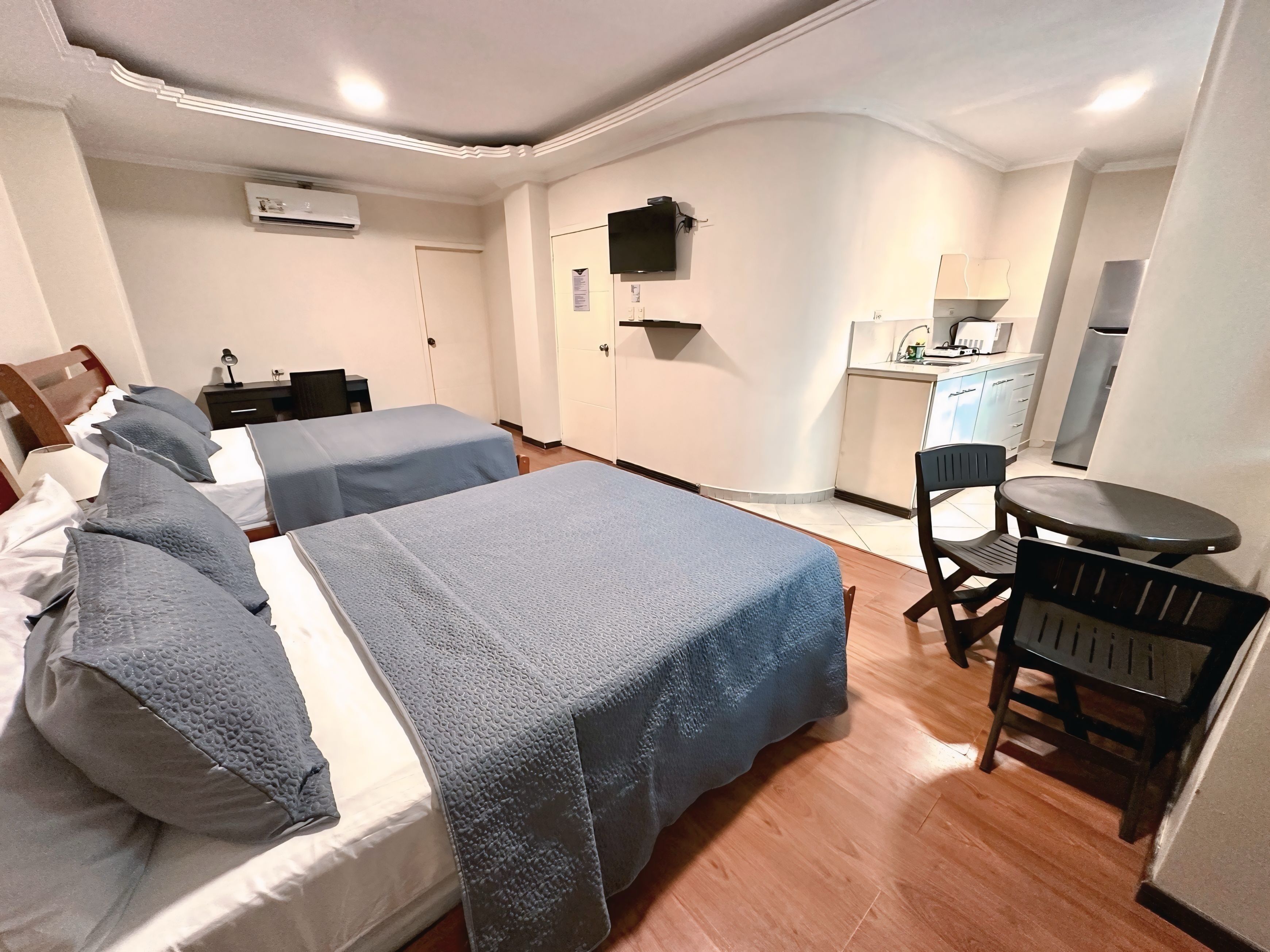 A hotel room with two beds, a desk, a chair, a TV, and a kitchenette.