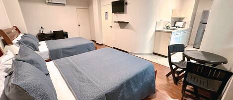 Habitación de hotel con dos camas, un escritorio, una silla, un televisor y una kitchenette.