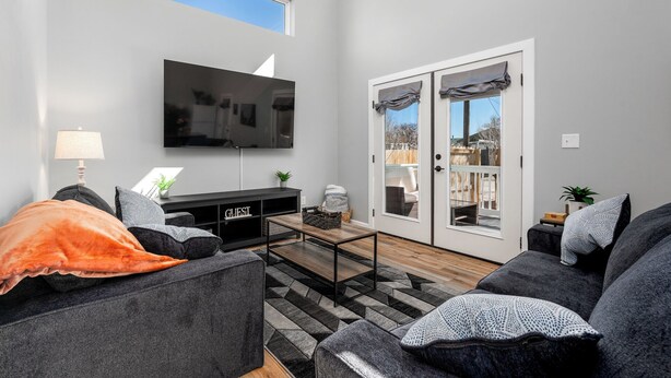 A modern living room with a flat-screen TV, grey sofas, a coffee table, and a sliding glass door leading to an outdoor area. - Hot Tub / Near Downtown / A/C / Couples Retreat (Colorado Springs)