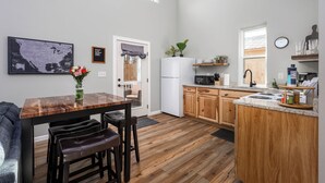 A modern kitchen with wooden cabinets, a white refrigerator, a microwave, and a dining area with a wooden table and leather chairs. - Hot Tub / Near Downtown / A/C / Couples Retreat (Colorado Springs)