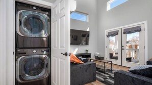 A laundry room with two stacked washers and dryers, a television, and a sliding glass door leading to a patio. - Hot Tub / Near Downtown / A/C / Couples Retreat (Colorado Springs)