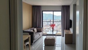 Una habitación de hotel moderna con un balcón grande, un sofá, una mesita y un televisor.