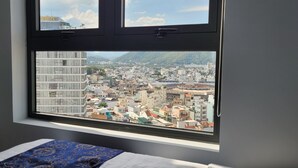 Una habitación con un ventanal grande que ofrece vistas a un paisaje urbano con edificios y montañas.