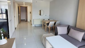 Una sala moderna con un sofá gris, una mesa de centro blanca y un comedor con una mesa y sillas de madera.