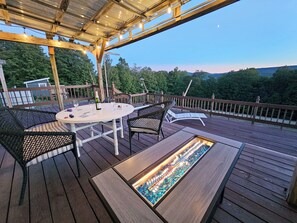Terraza de madera con una mesa redonda y sillas, una chimenea integrada y vistas del paisaje circundante.