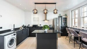A modern kitchen with a central island, black countertops, stainless steel appliances, and pendant lighting. - 3 Bdm Flat w/ HotTub and RoofTop (Greater London)