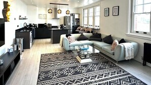 A modern kitchen with a central island, a dining area with a light blue sofa, and a patterned rug. - 3 Bdm Flat w/ HotTub and RoofTop (Greater London)