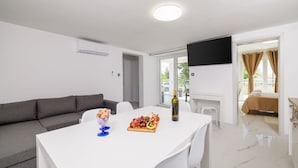 A modern living room with a white table set for dining, a grey sofa, and a flat-screen TV mounted on the wall. - Large pool with salt electrolysis not far from the healing mud bay (Kras-Dobrinj)