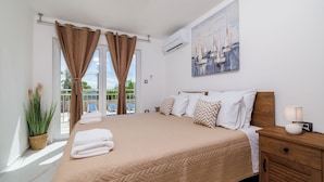 A bedroom with a large bed, a wooden nightstand, a wall-mounted air conditioner, and a painting of sailboats. - Large pool with salt electrolysis not far from the healing mud bay (Kras-Dobrinj)