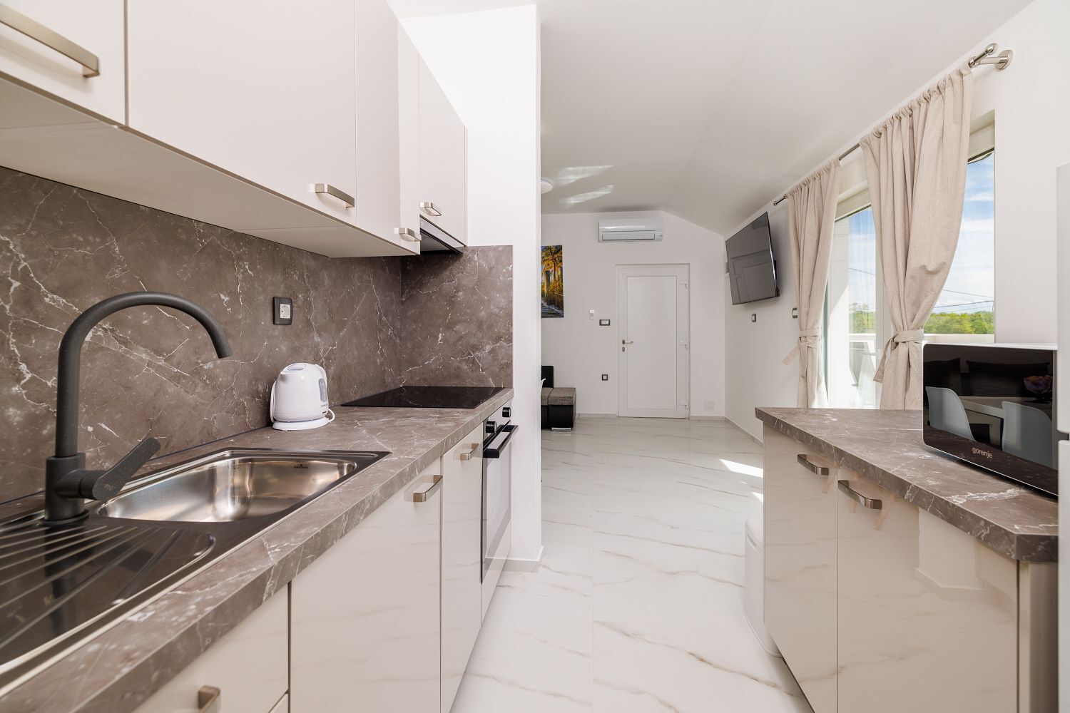 A modern kitchen with a marble countertop, stainless steel sink, and a built-in oven.