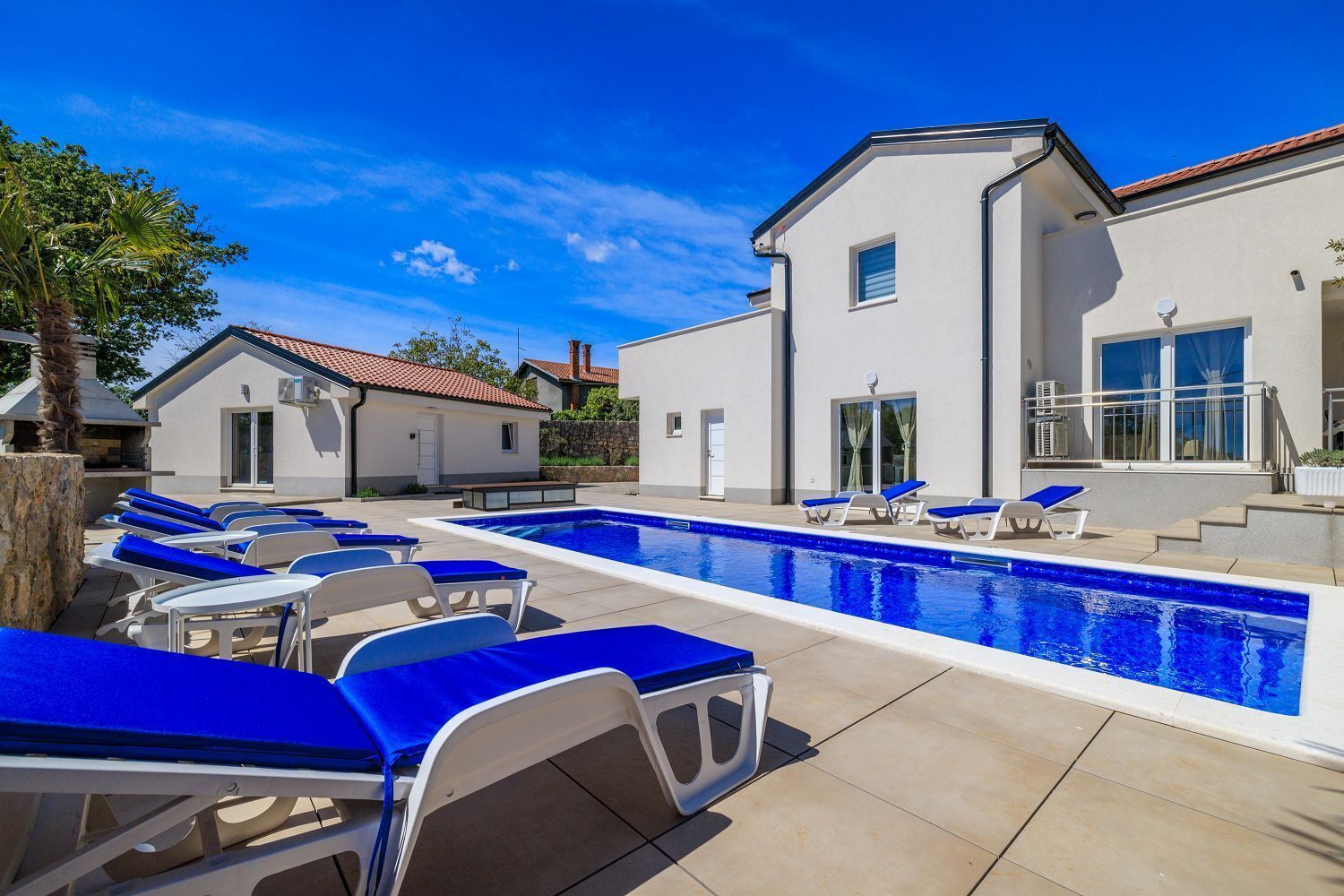 A pool area with lounge chairs and a modern building with a tiled roof.