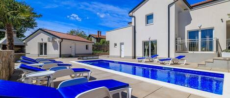 A pool area with lounge chairs and a modern building with a tiled roof.