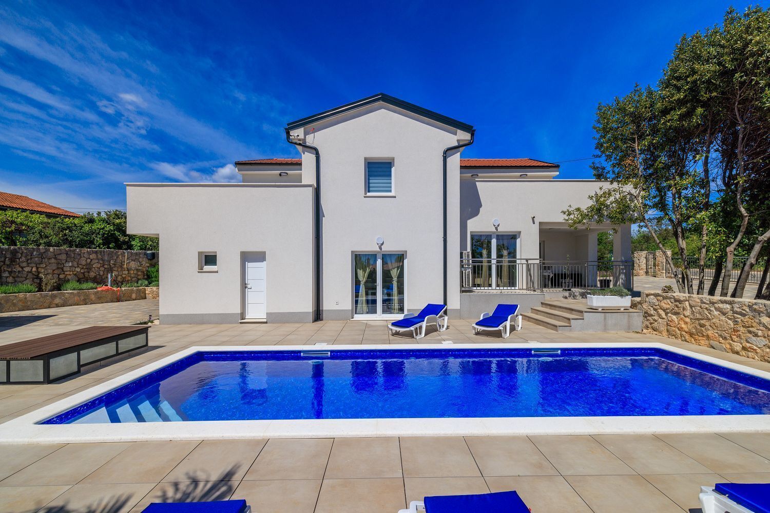 Una casa moderna de dos pisos con piscina, un muro de piedra y un espacio de patio cubierto.