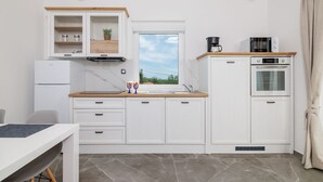 Una cocina compacta con armarios blancos, horno empotrado, microondas y ventana con vistas al verdor.