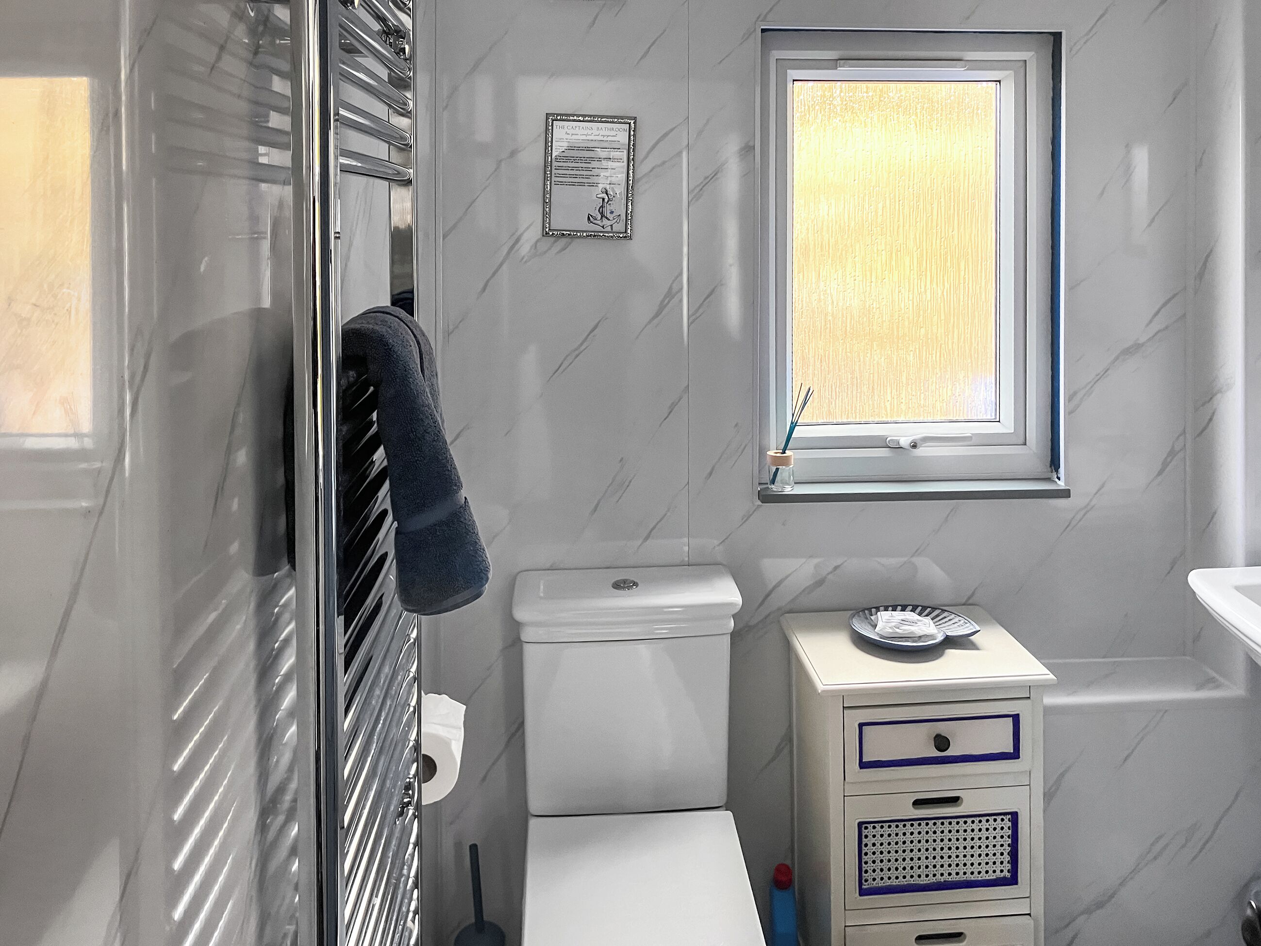 A bathroom with a toilet, a window, a towel rack, and a cabinet with drawers.