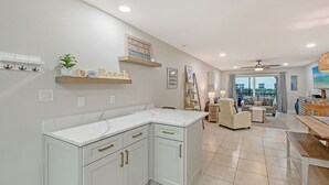 A modern kitchen with white cabinetry and a marble countertop, leading to a living area with a sofa and a dining table. - 3 min. walk to Siesta Key Beach-NEWLY RENOVATED 1st floor 2BR/2B w/ heated pool (Siesta Key)