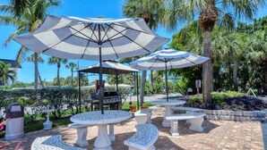 Outdoor seating with umbrellas, a grill, and palm trees. - 3 min. walk to Siesta Key Beach-NEWLY RENOVATED 1st floor 2BR/2B w/ heated pool (Siesta Key)
