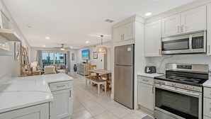 A modern kitchen with white cabinets, stainless steel appliances, and a dining area with a table and chairs. - 3 min. walk to Siesta Key Beach-NEWLY RENOVATED 1st floor 2BR/2B w/ heated pool (Siesta Key)