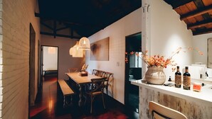 Un coin repas avec une table et des chaises en bois, un luminaire suspendu et un vase rempli de fleurs posé sur le comptoir.