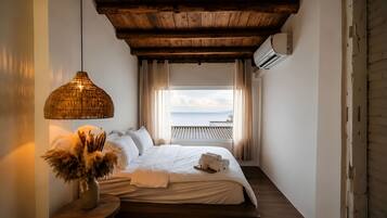 A bedroom with a bed, a hanging lamp, a view of the sea, and a wooden ceiling.