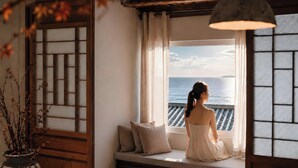 Une chambre avec vue sur la mer, un paravent traditionnel en bois et une plante en pot.