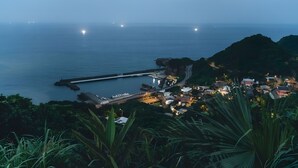 Une ville côtière au crépuscule, avec une jetée, des maisons et une végétation luxuriante.