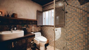 Une salle de bain avec un mur en pierre, un lavabo blanc, des toilettes et un espace douche.