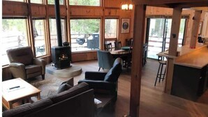 A cozy cabin interior with a fireplace, wooden furniture, and large windows. - Bear Valley Alpine Cabin-3bdrm2bth (Bear Valley)