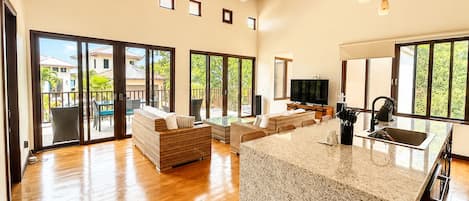 A spacious living area with a kitchen island, sliding glass doors to a balcony, and a ceiling fan.