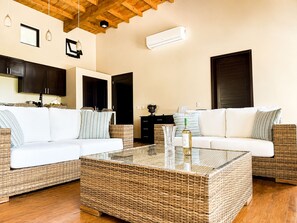 A modern living room with a glass coffee table, white sofas, and wicker furniture. - Living Waters Casita  Private Pool, Camp Bay (Camp Bay)