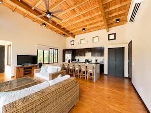 A spacious living area with a high ceiling, a television, a sofa, and a kitchen area with bar stools. - Living Waters Casita  Private Pool, Camp Bay (Camp Bay)