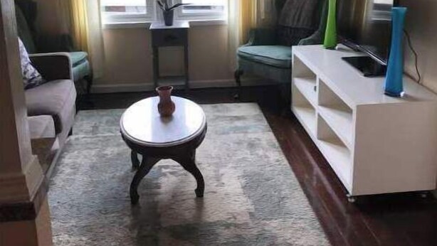 Una sala de estar con sofá, mesa de centro, mueble para televisión y ventana con cortinas.