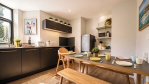 A modern kitchen with dark cabinets, a wooden dining table, and a bench. - 3BR Westbourne Delight - Near Beach & Bournemouth! (Bournemouth)