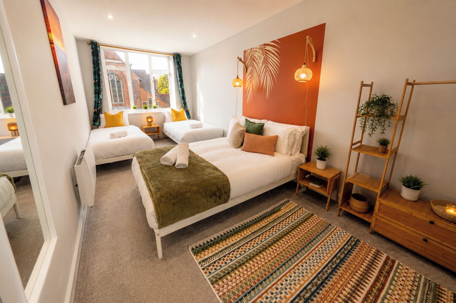 Quarto moderno com uma cama grande, um sofá-cama menor, uma mesinha de cabeceira de madeira, um abajur e uma prateleira na parede com plantas.