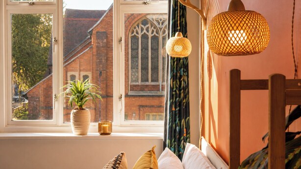 A room with a large window, a potted plant, a wooden chair, and a hanging light fixture. - 3BR Westbourne Delight - Near Beach & Bournemouth! (Bournemouth)