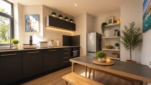 A modern kitchen with dark cabinets, a wooden bench, and a dining table. - 3BR Westbourne Delight - Near Beach & Bournemouth! (Bournemouth)